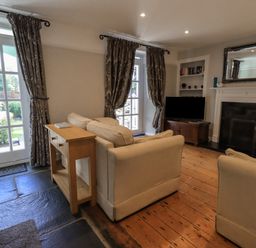 A living room with beige sofas a wooden console table a fireplace and a television at Brook Cottage in Windermere