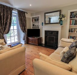 A living room with two beige sofas a fireplace a television bookshelves and patterned curtains at Brook Cottage in Windermere