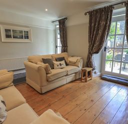 A living room with two beige sofas a small wooden stool and glass doors with curtains at Brook Cottage in Windermere