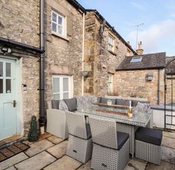 An outdoor patio area with wicker furniture and glass table in front of a stone house at Market Square Maisonette in Kirkby Lonsdale