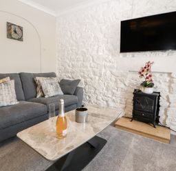 A living room with a gray sofa a marble coffee table a wall-mounted television and a small stove with flowers at Market Square Maisonette in Kirkby Lonsdale