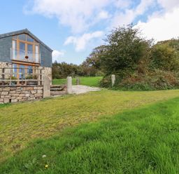 A stone and wood house with a balcony and garden surrounded by grass and trees at The Orchard in Cardinham