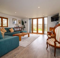 A living room with teal sofas a wooden coffee table and glass doors leading outside at The Orchard in Cardinham