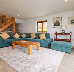 A living room with a teal sectional sofa and wooden coffee table near a wooden staircase at The Orchard in Cardinham