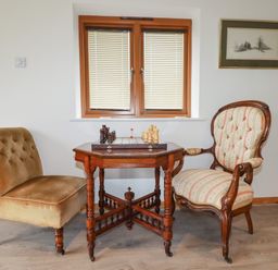 A room with two chairs and a wooden table with a chess set under a window at The Orchard in Cardinham