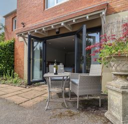 An outdoor patio with table and chairs next to open glass doors and a large planter at The Hideaway in Uplyme near Lyme Regis
