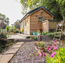 A wooden cabin with a small garden path and potted plants at Chateau Petit in Trefeglwys