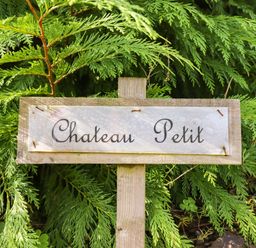 A wooden sign with the words Chateau Petit in front of green leafy plants at Chateau Petit in Trefeglwys