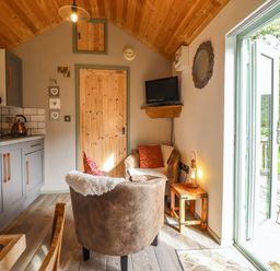 A small kitchen and seating area with two armchairs a wall-mounted TV and glass doors leading outside at Chateau Petit in Trefeglwys
