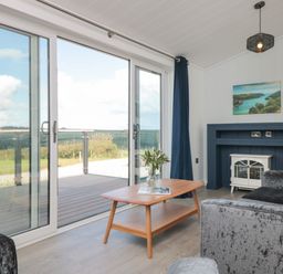 A living room with glass sliding doors a wooden coffee table and a small fireplace at Buttercup Lodge in Norton near Dartmouth