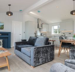 An open living room and kitchen with blue velvet sofas a wooden coffee table and dining table at Buttercup Lodge Norton near Dartmouth