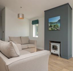 A living room with two beige sofas a gray fireplace with a white stove and a window with a green blind at Primrose Lodge in Norton near Dartmouth