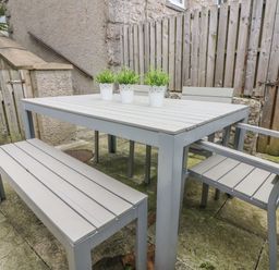 An outdoor dining area with a rectangular table, bench, chairs, and three potted plants on the table at Church View in Grange-Over-Sands