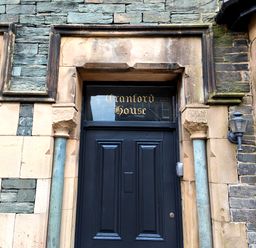 Black door with gold lettering Cranford House above in a stone building with decorative pillars and a wall lantern at Cranford House Keswick