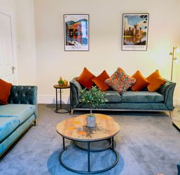 A living room with blue sofas and orange cushions a round wooden coffee table with a plant and wall art at Cranford House in Keswick