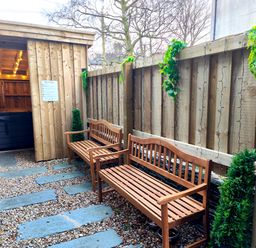 An outdoor seating area with two wooden benches stone pathway wooden fence and a covered hot tub at Cranford House in Keswick