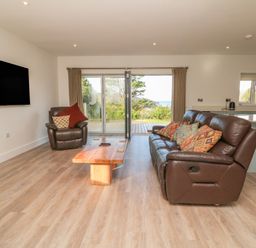 A living room with brown leather sofas a wooden coffee table a wall mounted tv and sliding glass doors opening to a garden at Linden View in Combe Martin