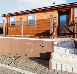 An exterior view of a brown mobile home with stairs leading to a porch enclosed by a glass railing at Serenity Sunset in Ilfracombe