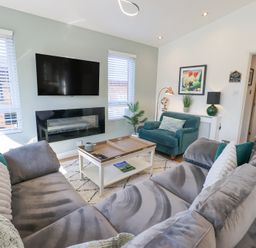 A living room with a gray sectional sofa a green armchair a white coffee table and a wall-mounted TV at Tranquil Waters Lakeside 16 White Cross Bay near Windermere