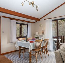 A dining room with a table set for four near windows and a sliding door at Teign River Retreat in Drewsteignton near Moretonhampstead
