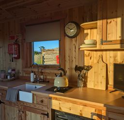 A kitchen area with a sink kettle utensils clock and small tv at Hafan Gelli Sheperds Hut - Enlli in Pwllheli