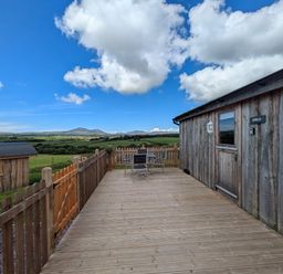 An outdoor wooden deck with table and chairs beside a wooden building at Hafan Gelli Sheperds Hut - Enlli in Pwllheli