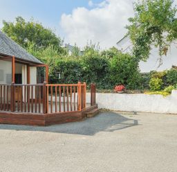 An outdoor area with a small wooden deck and railing next to a white wall with plants and flowers at Little Trevallan in Looe