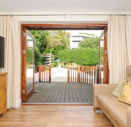 A living room with a leather sofa and wooden cabinet next to open double doors leading to a deck at Little Trevallan in Looe