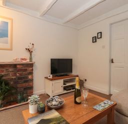 A living room with a wooden coffee table holding plants a bottle of cava and two glasses next to a beige sofa at Shell Seeker Cottage in Sewerby