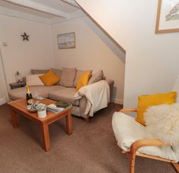A living room with a sofa, armchair, wooden coffee table, and wall art at Shell Seeker Cottage in Sewerby