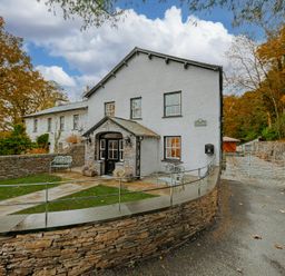 The exterior of a white house with stone walls and a pathway surrounded by trees at Gate House in Coniston