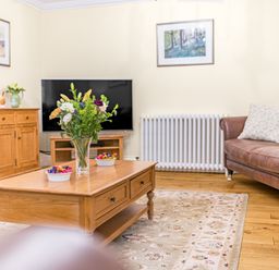 A living room with a wooden coffee table with flowers on it and a television at Gate House in Coniston