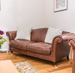 A leather sofa with cushions in a living room with wooden floor and a table with flowers at Gate House in Coniston
