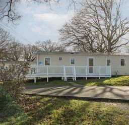 A beige mobile home with white railings and steps in a wooded area at 15 Rosewood Great Thorness near Northwood Isle Of Wight
