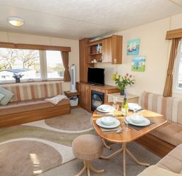 A living area with a dining table set for four a television and cushioned seating at 15 Rosewood Great Thorness near Northwood Isle Of Wight