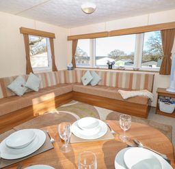 A seating area with striped cushions and pillows around windows with curtains next to a dining table set with plates and glasses at 15 Rosewood Great Thorness near Northwood Isle Of Wight