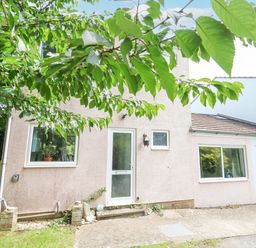 A house exterior with a door and several windows partially covered by tree branches at Mermaid Cottage in Wakeham Portland