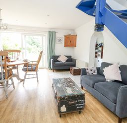 A living room with grey sofas and a wooden dining table near a sliding glass door at Mermaid Cottage in Wakeham Portland