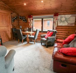 A living room with a dining table chairs an armchair and a sofa with red cushions at 10 Waters Edge Morpeth near Felton