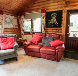 A living room with a red leather sofa and a gray armchair with red cushions at 10 Waters Edge Morpeth near Felton