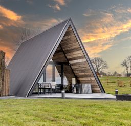An A-frame cabin with outdoor seating and wooden walls on a grassy area at The Tri-Pod in Pantcefn near Llanarth