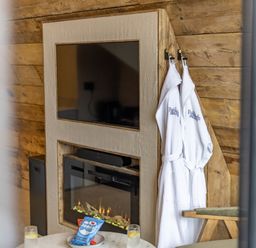 A wall-mounted television above a fireplace with two white robes hanging on hooks by a wooden wall at The Tri-Pod Pantcefn near Llanarth