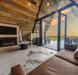 An interior living space with a fireplace a round table and brown sofa next to glass doors opening to an outdoor deck at The Tri-Pod in Pantcefn near Llanarth
