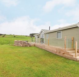 An exterior view of a single-story building with a wooden deck and glass railing on a grassy area at No.7 Skiddaw View in Moota near Aspatria