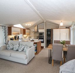 An open plan living room with a sofa, kitchen area with appliances, and dining table with chairs at No.7 Skiddaw View Moota near Aspatria