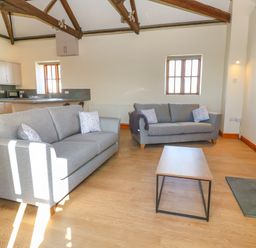 A living room with two grey sofas a wooden coffee table a wood stove and an open kitchen at The Granary in Prussia Cove near Rosudgeon