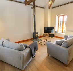 A living room with two grey sofas a wood burning stove a coffee table and a television at The Granary in Prussia Cove near Rosudgeon