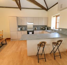 A kitchen with a breakfast bar and two stools next to a dining table with bench seating at The Granary in Prussia Cove near Rosudgeon