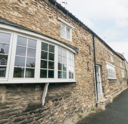 A stone building with white framed windows and a white door along a sidewalk at York House in Thornton Dale