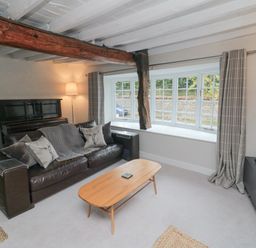 A living room with a leather sofa a wooden coffee table a piano and a large window at York House in Thornton Dale